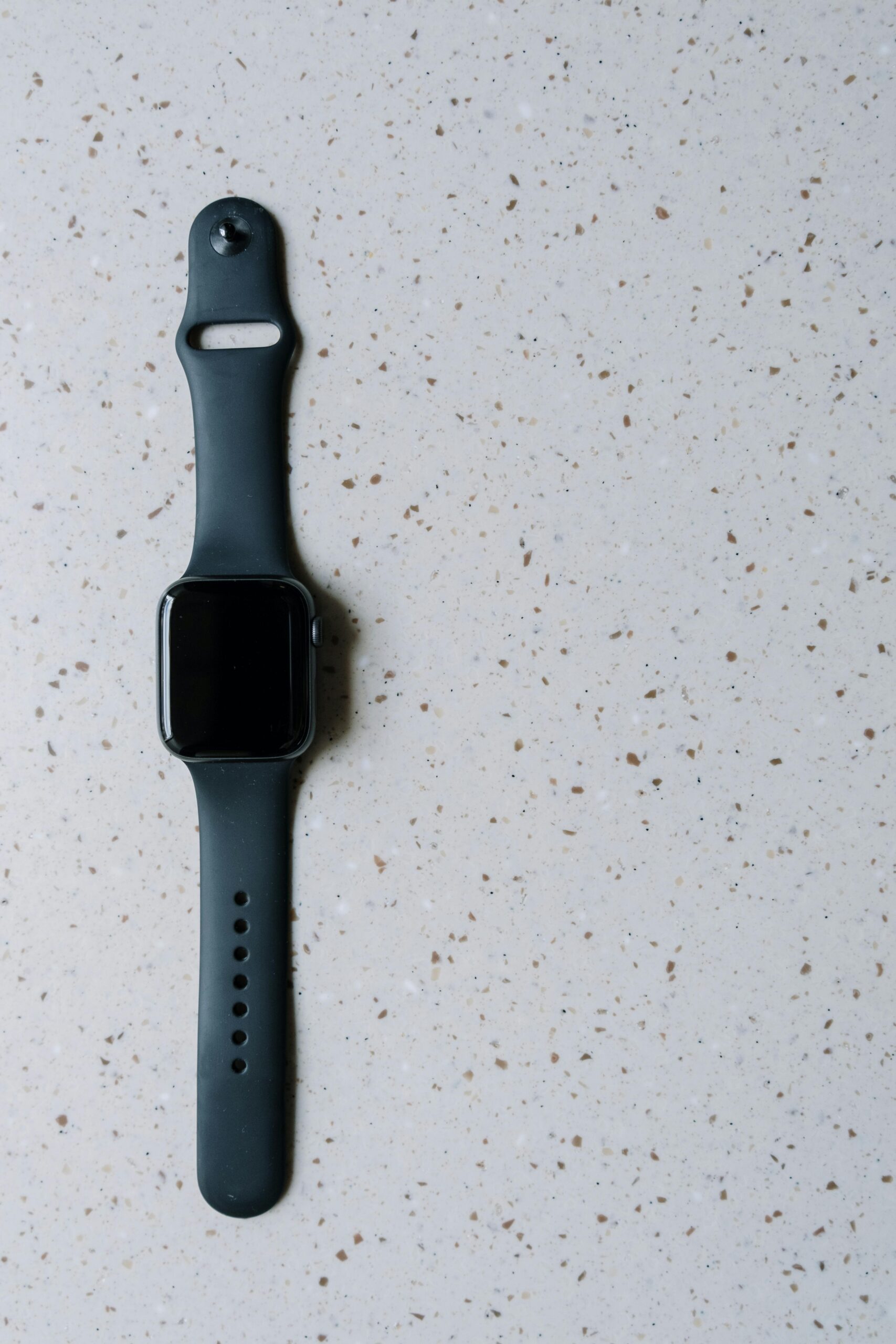 Flat lay image of a black smartwatch on a terrazzo surface, showcasing modern technology.