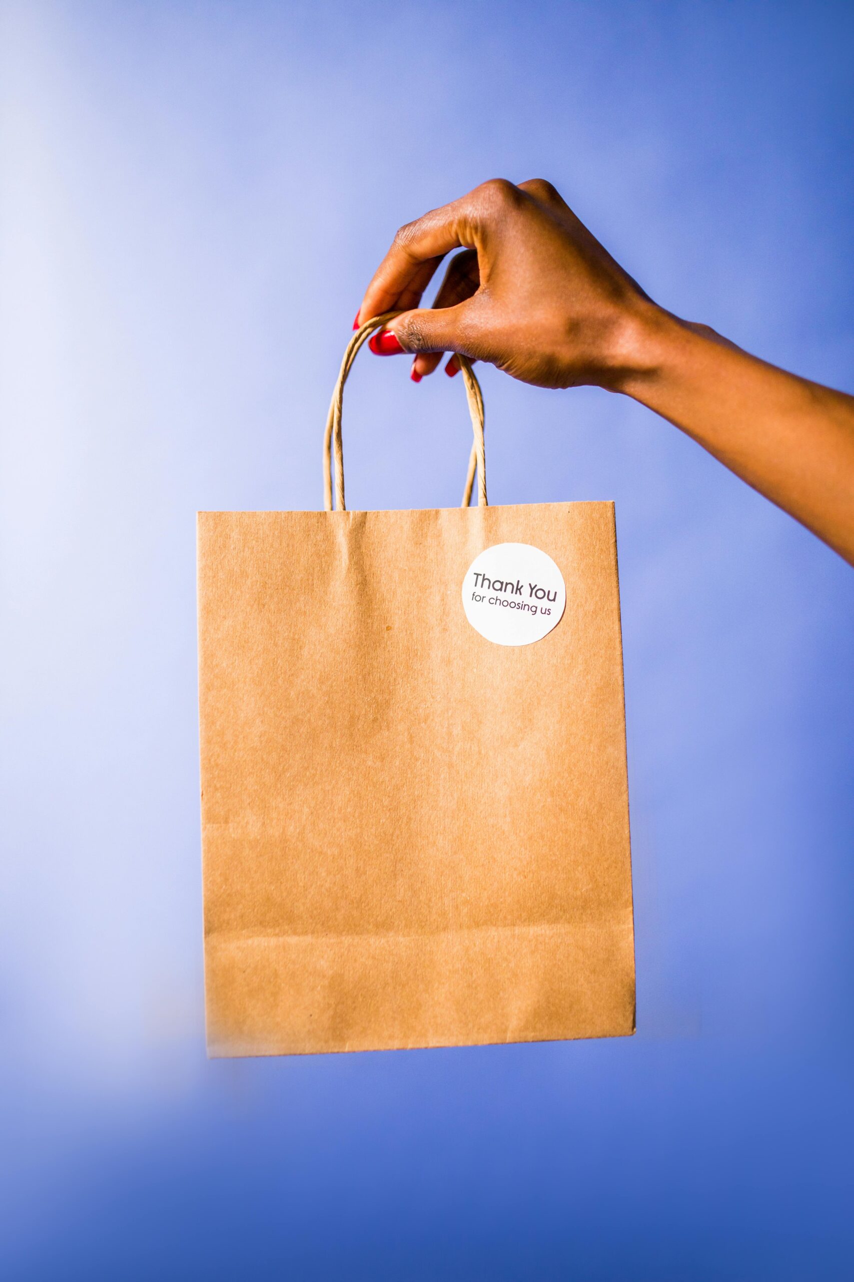 A hand holds a thank you paper bag against a vibrant blue background.