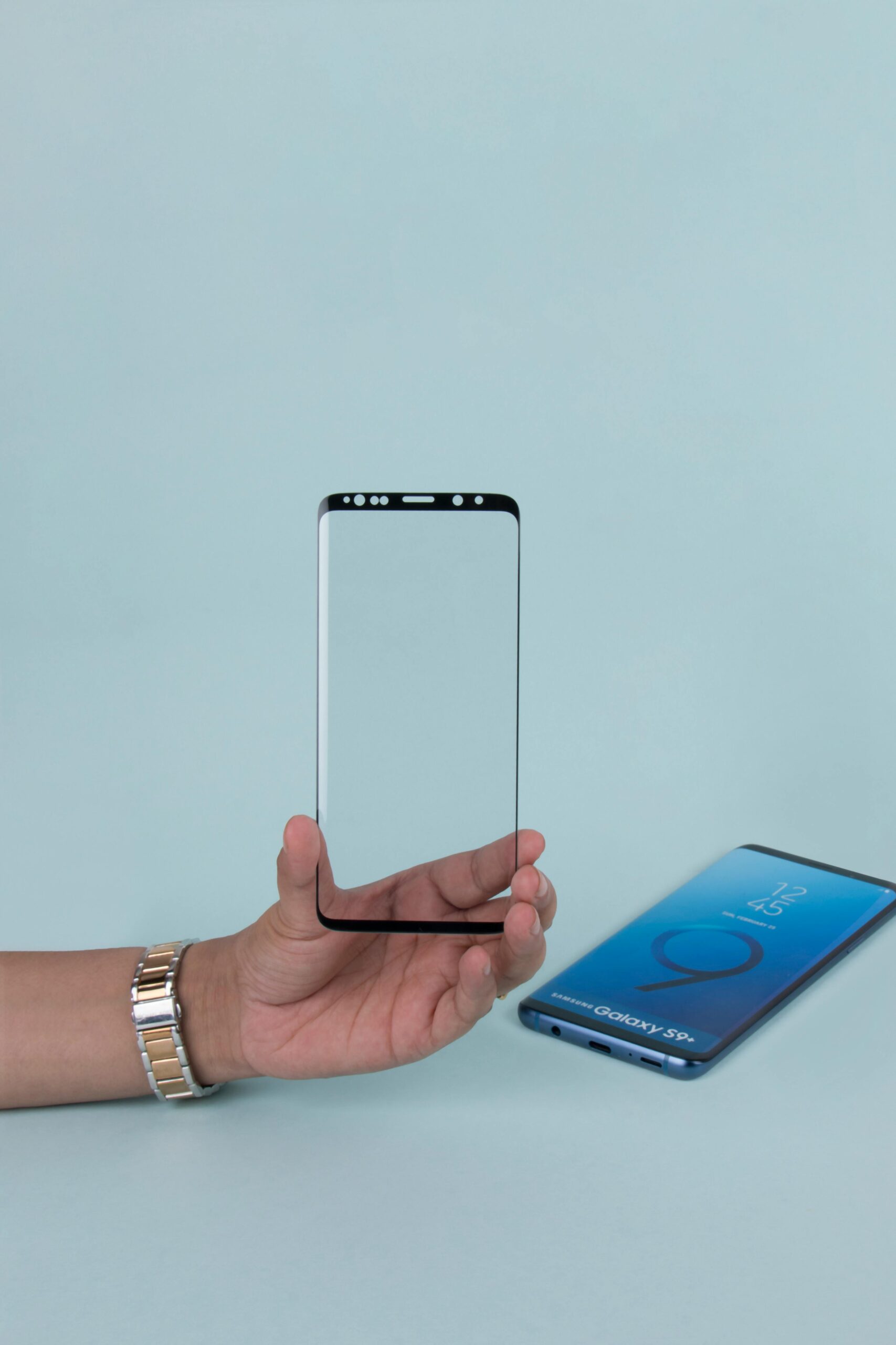 Close-up of a hand holding a transparent phone screen protector against a blue background.